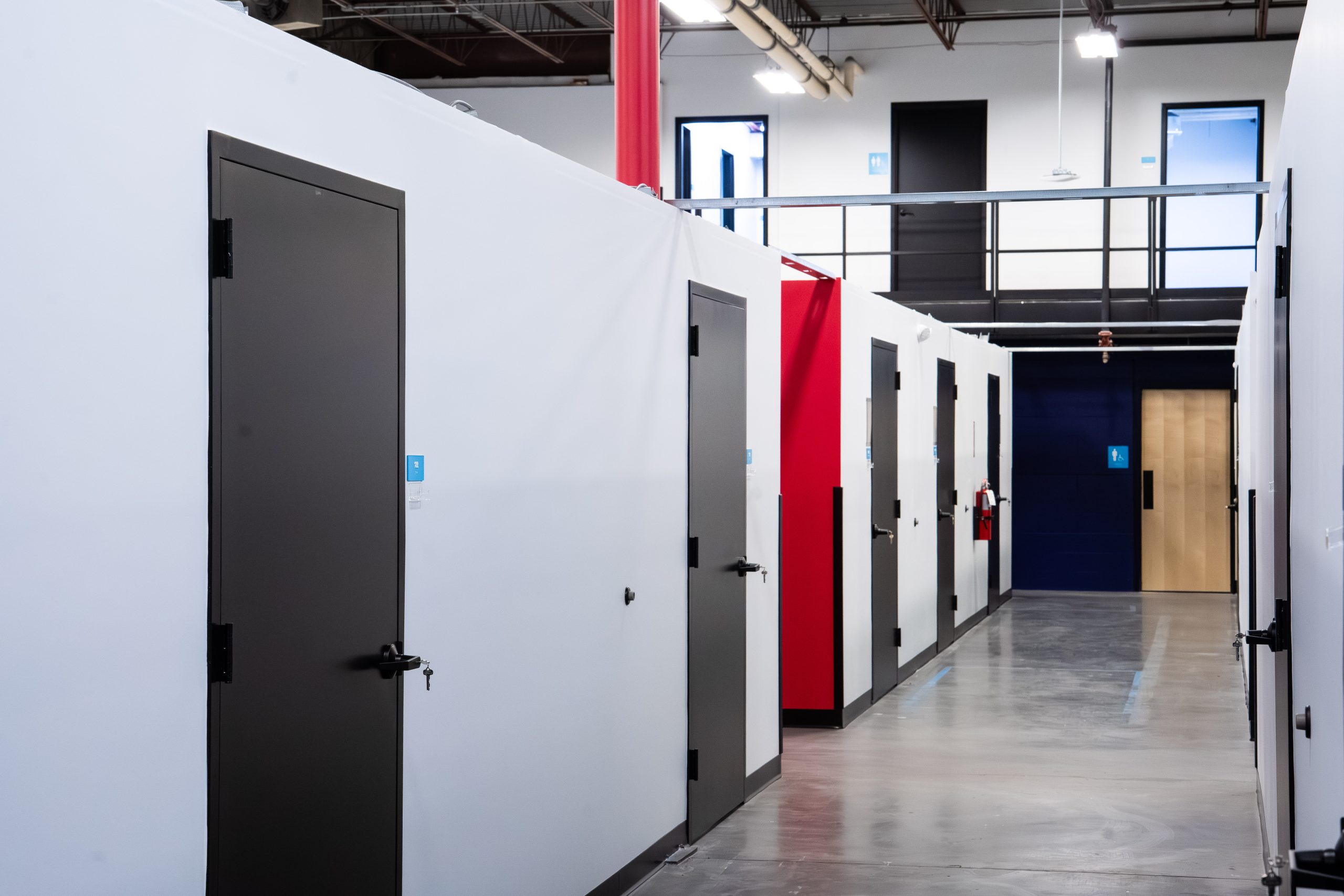 Private warehouse storage units at Elevator Co-Warehousing in North Kansas City with secure black doors, polished concrete floors, wide corridors, and modern industrial design with red and blue accent walls.