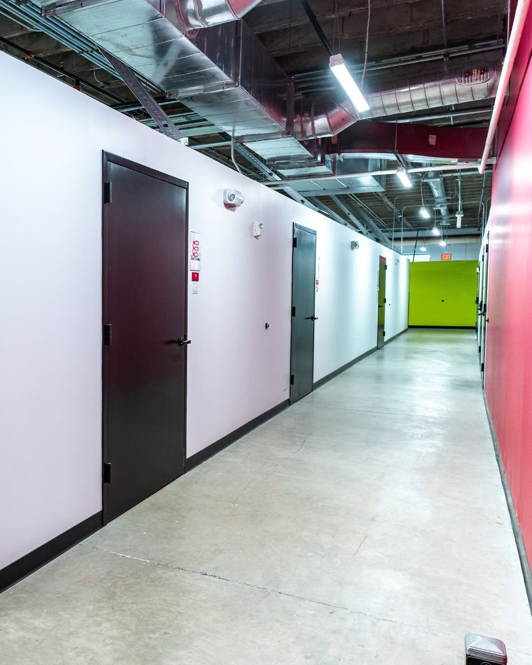 Hallway lined with private warehouse unit doors, industrial ceiling, and bold red and green accent walls at an Elevator location